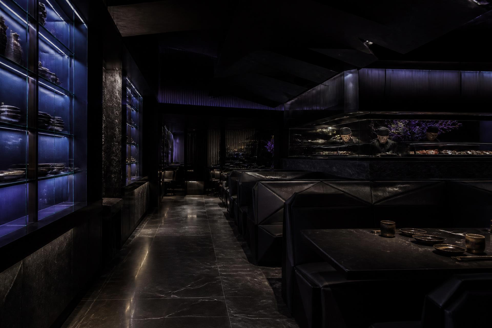 Dunkles, blau beleuchtetes Restaurant-Interieur mit schwarzen geometrischen Sitznischen